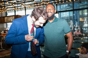 Two people sharing a lighthearted moment at a bar with string lights overhead.