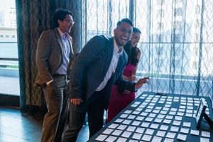 Three attendees interact by a window during a professional networking event.