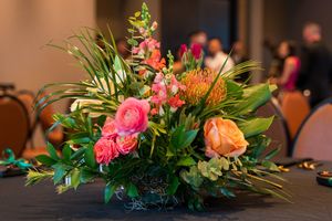 Tropical floral centerpiece with pink roses and orange protea blooms on dark table.