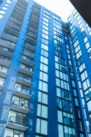 Modern blue high-rise apartment building with glass windows and balconies photographed from below.