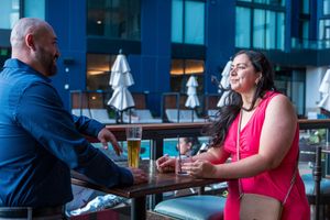 Two people enjoy drinks while socializing at outdoor patio table.