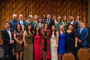 Large group photo at a formal event with people wearing cocktail attire against a wooden wall backdrop.