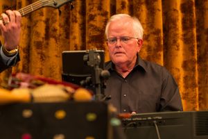 Sound technician operates audio equipment in front of orange curtain during performance.