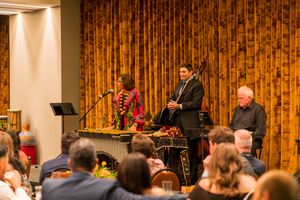 Musicians performing on stage with wooden paneling and audience in view.