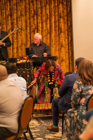 Musicians perform on percussion instruments against golden curtains at an indoor venue.