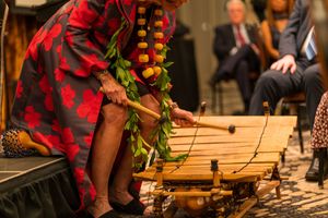 Musician playing a wooden xylophone instrument while wearing traditional red dress.