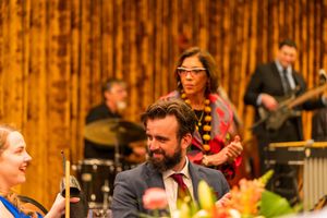 Musicians perform with guitars and instruments against a wood-paneled backdrop at an evening event.