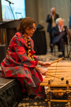 Musician in red floral dress plays traditional wooden xylophone instrument during performance.