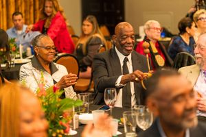 Audience members engage enthusiastically during an indoor event in a formal banquet setting.