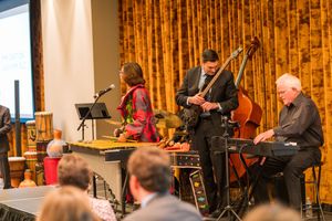 Musicians performing on stage with instruments in front of gold curtained backdrop.