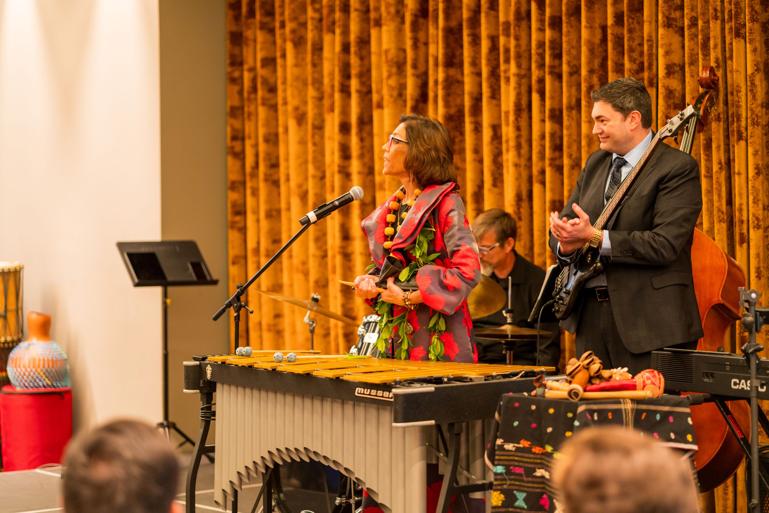 Musicians performing on stage with marimba and guitar at a jazz concert with orange curtain backdrop.