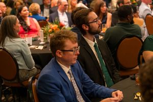 Attendees in business attire listen intently during a conference presentation.