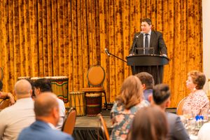 Speaker delivering presentation at podium in front of bamboo wall during professional business event.