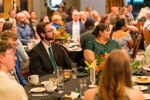 Engaged audience members seated at round tables during a formal dinner event.