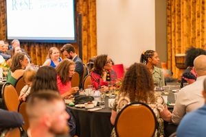 Guests enjoy a formal dinner event in a ballroom with orange curtained walls.