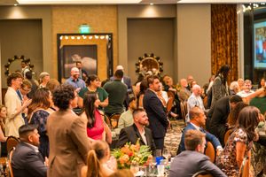 Large crowd gathered in a banquet hall for an event with decorative lighting.