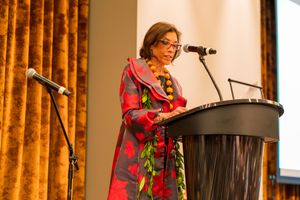 Speaker presenting at a podium in front of golden curtains during a formal event.
