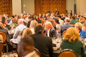 Large crowd of attendees seated at round tables during formal banquet dinner event.