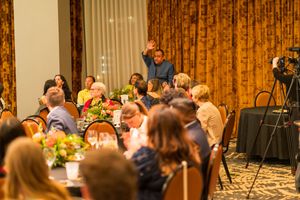 Guests seated at decorated banquet tables during an indoor event with golden curtains in the background.