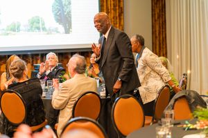 A celebration event in an indoor venue with guests sitting at round tables while someone presents at the front.