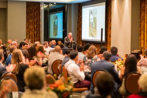 Wide shot of formal event space with projection screens and attendees seated at dining tables.