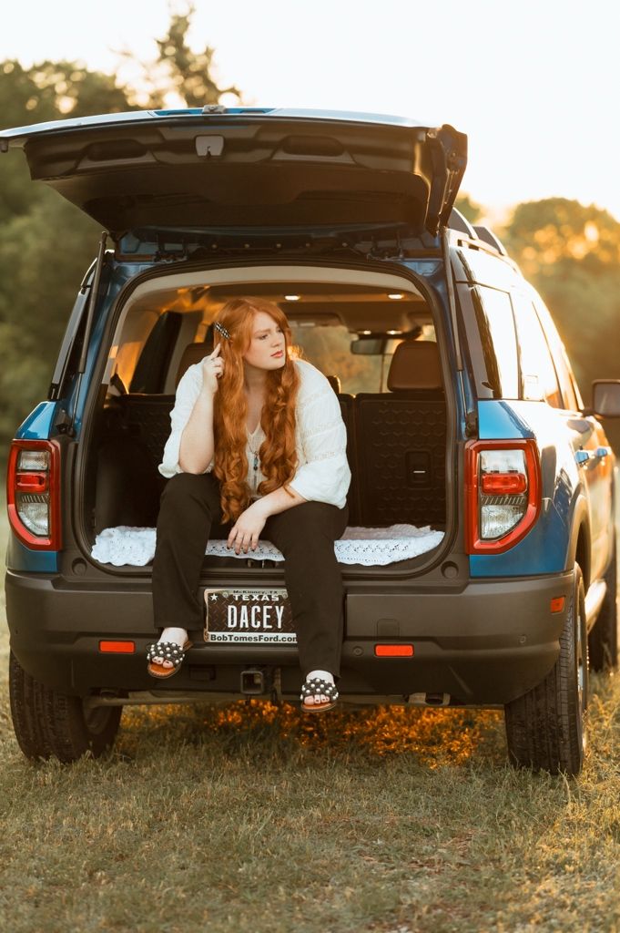Someone sits in the open trunk of a black SUV at sunset in a golden field with warm lighting.