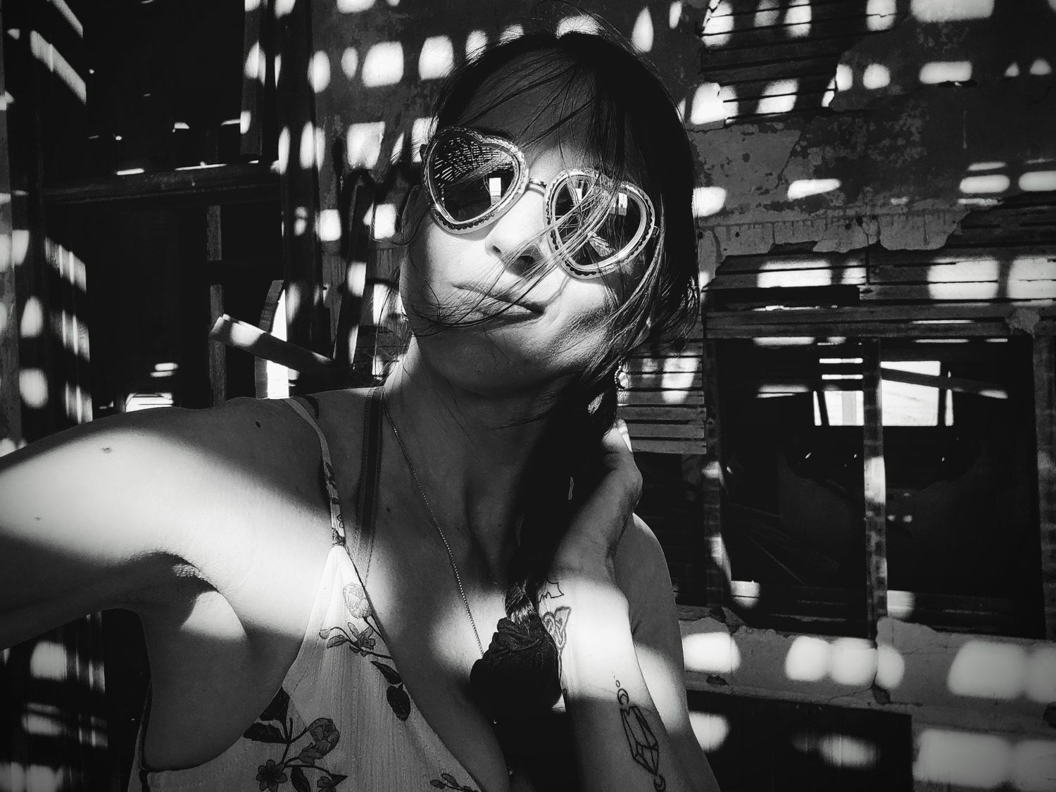 A black and white artistic photograph shows someone wearing round sunglasses in an urban nighttime setting.
