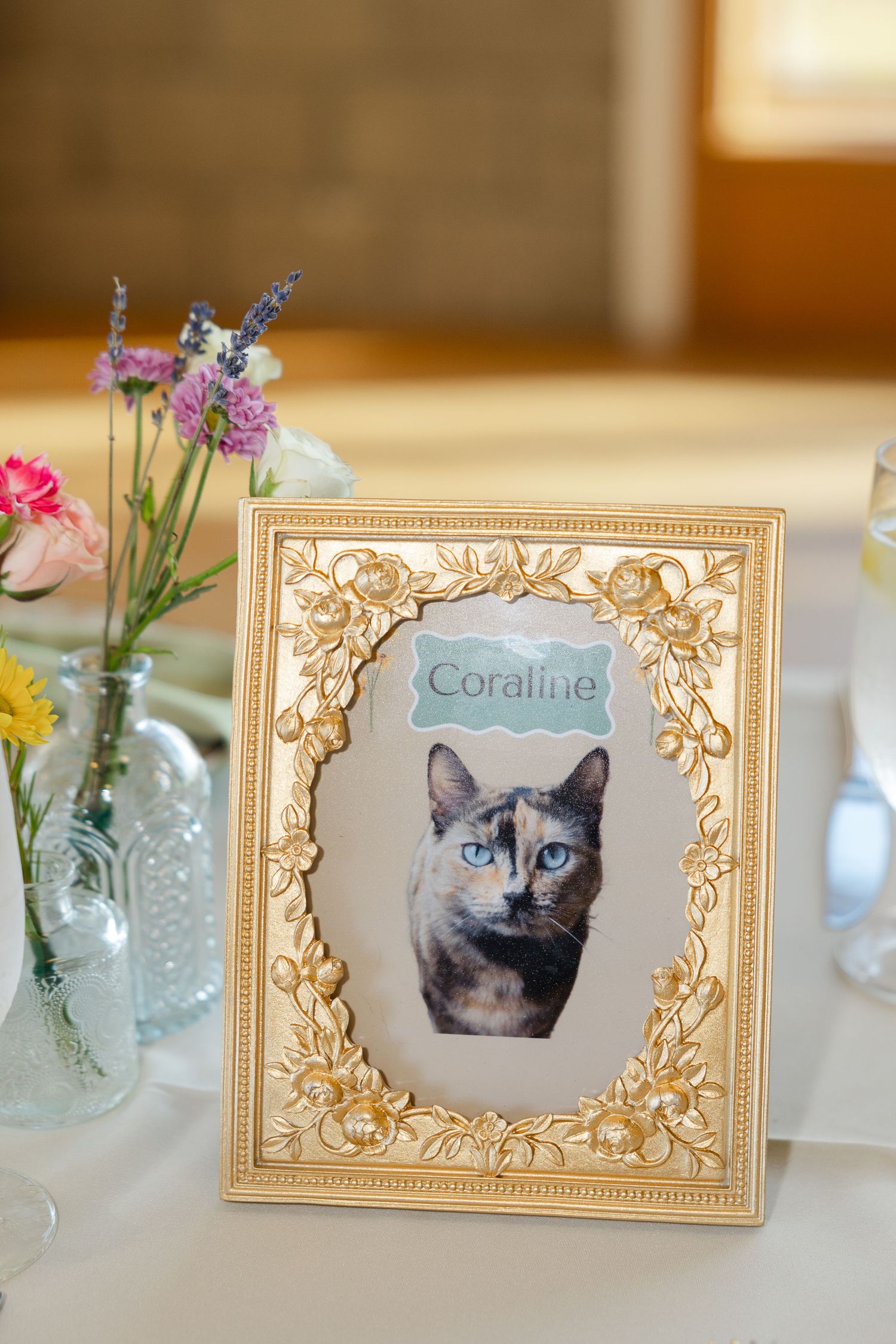 Elegant gold frames displaying cat portraits alongside delicate flower arrangements in glass vases at a table setting.
