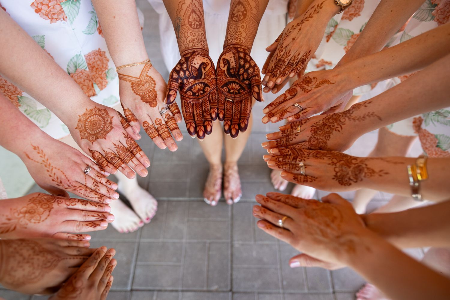 Top-down view of hands decorated with intricate henna designs forming a circle on tile floor.