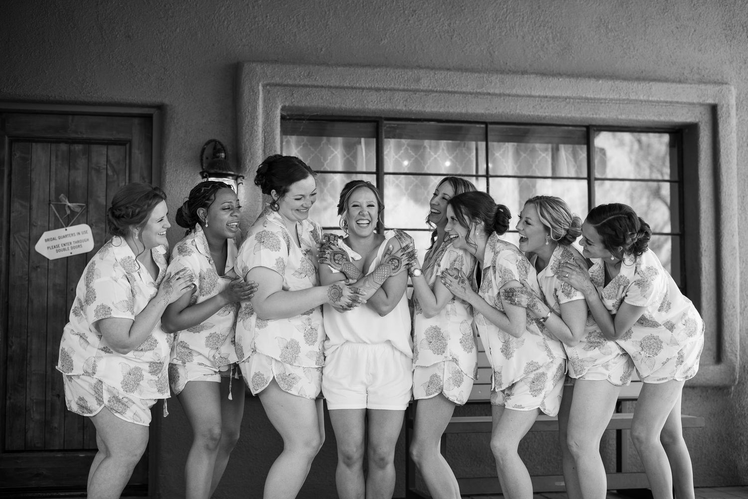 Bridesmaids in matching white robes laughing together before a wedding ceremony.