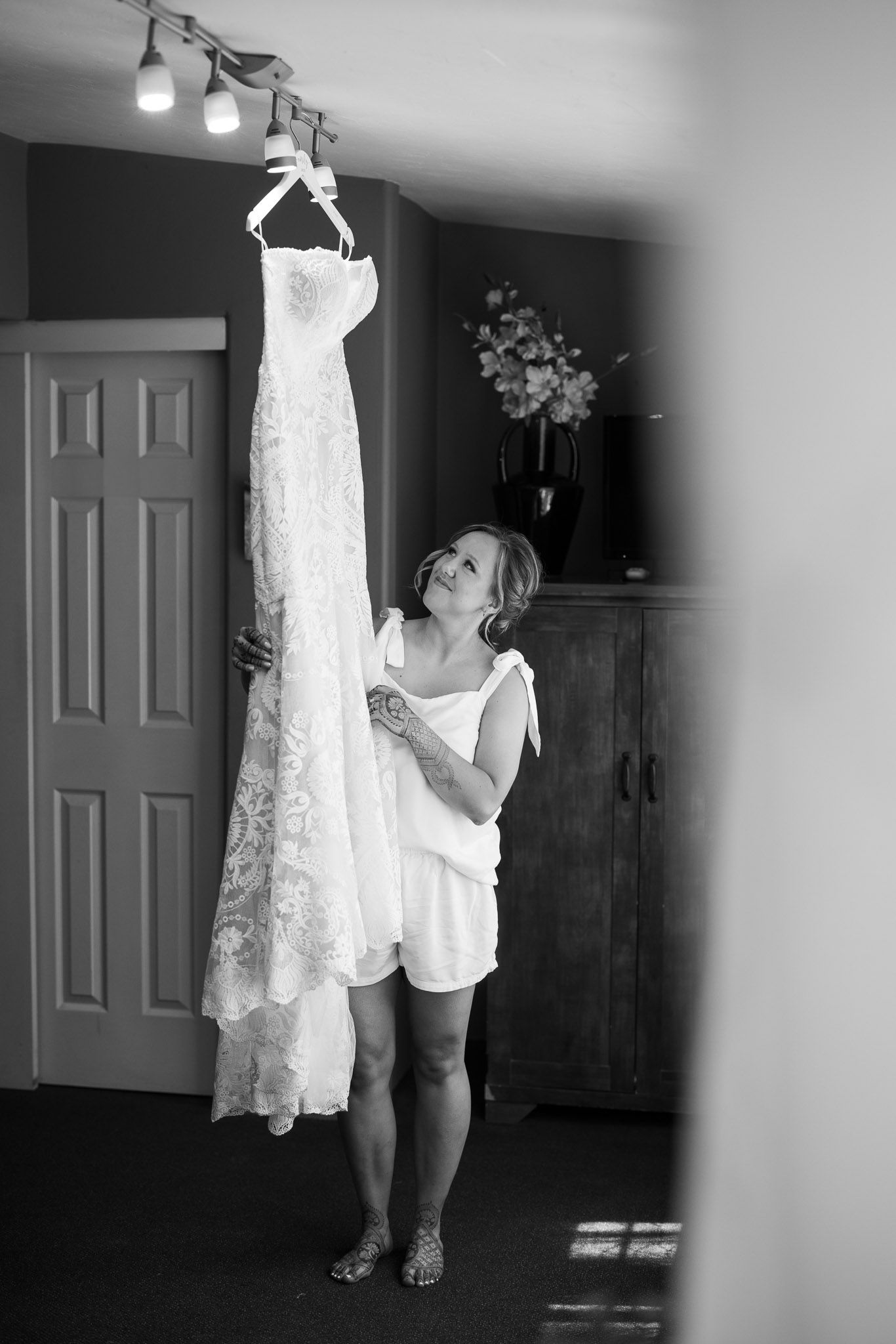 A white lace wedding dress hangs from a curved track light as someone inspects the delicate details.