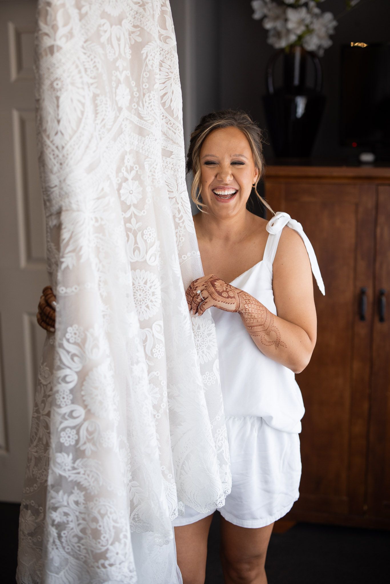 Wedding dress details showing delicate lace against white curtains in natural light.