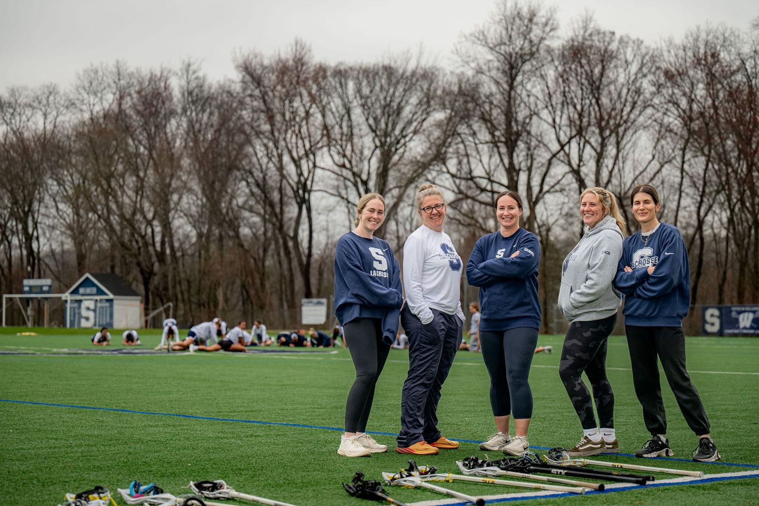 Athletes gather on artificial turf field during outdoor practice session in early spring weather conditions.