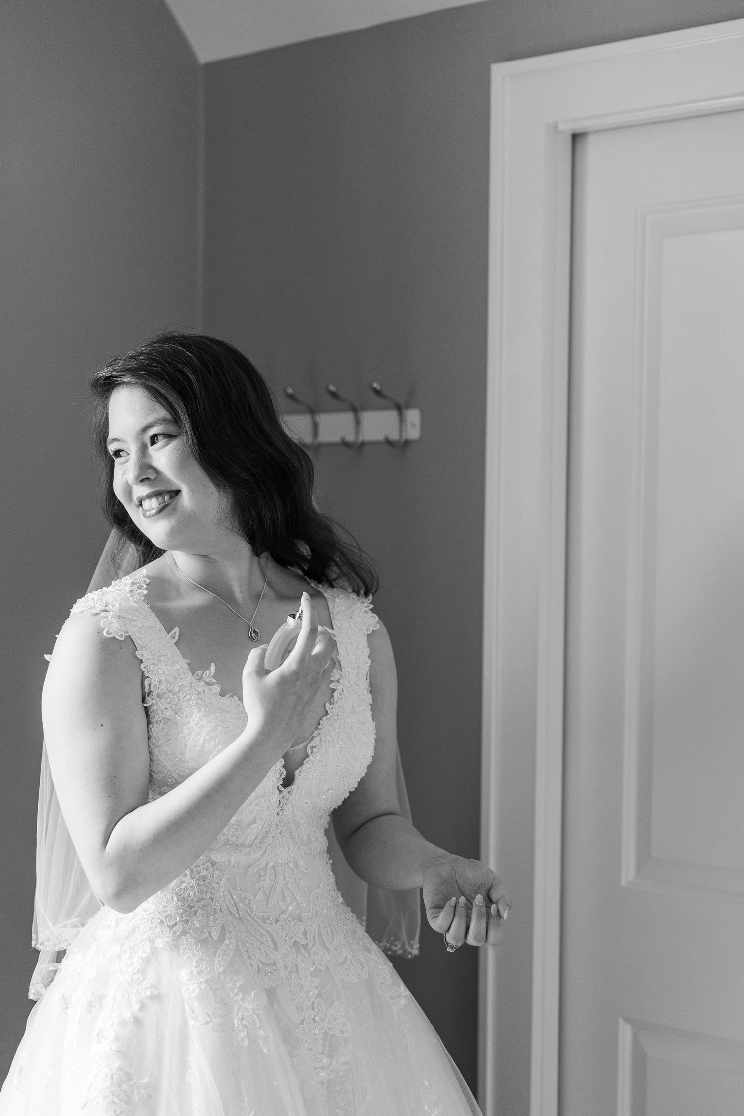 Black and white photograph of a bride in a lace wedding dress smiling while looking to the side in a room.