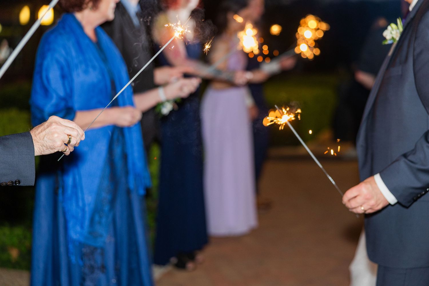 Wedding guests holding sparklers creating a magical nighttime celebration atmosphere at an outdoor reception.