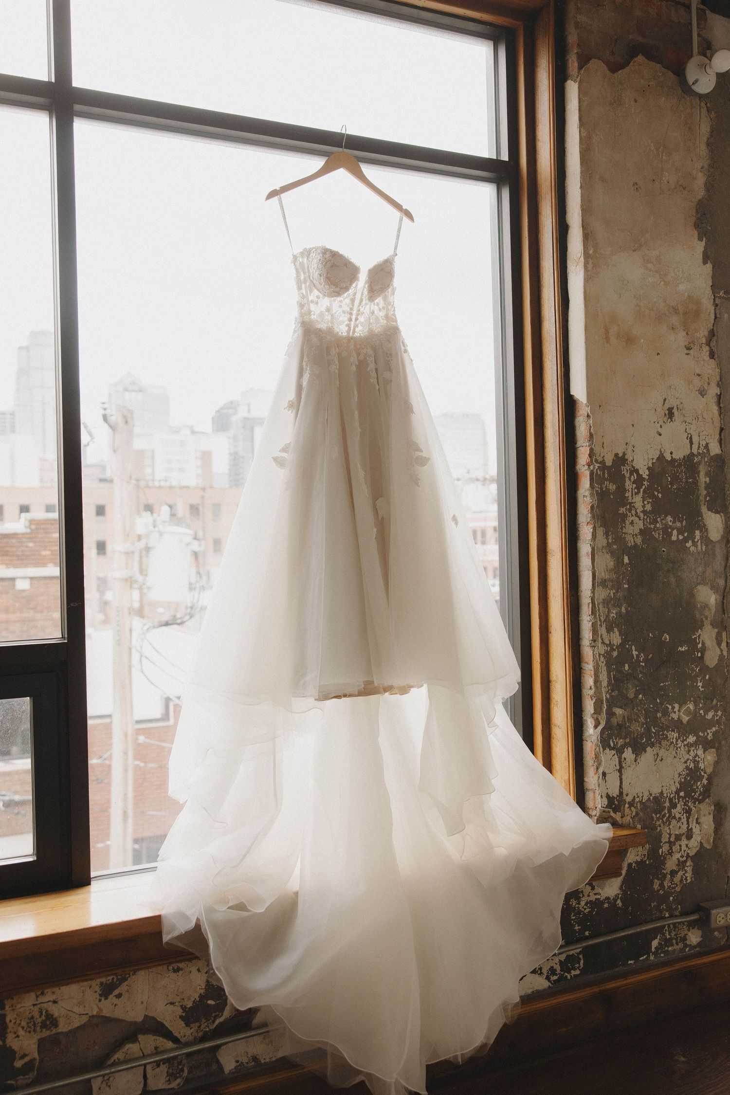 White wedding dresses hanging by windows in a rustic industrial space with natural light streaming in.