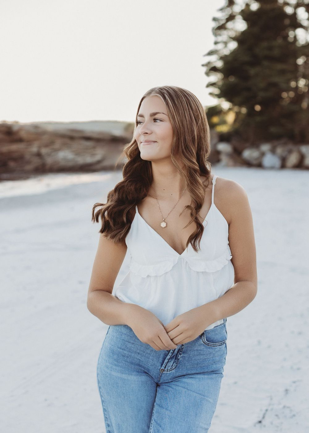 Senior girl laughing while walking along the shoreline during golden hour beach photo session in Maine.