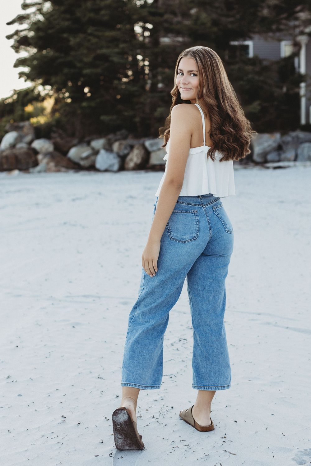 Natural, candid portrait of a high school senior with windblown hair standing in the sand dunes near the ocean.