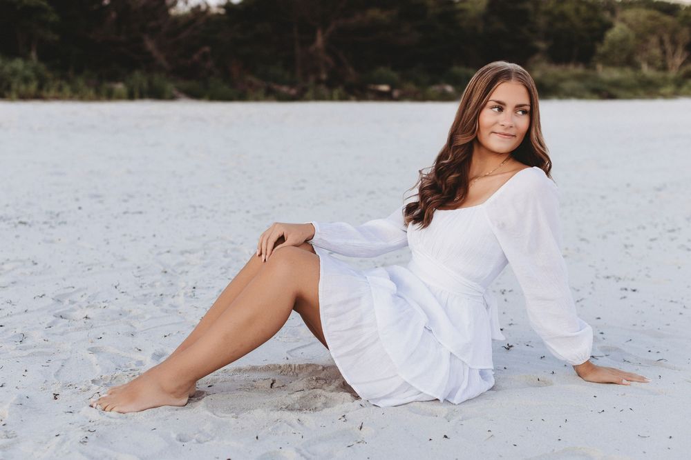 Senior posing confidently in a sundress with waves crashing behind her during a sunset beach photography session in Maine.
