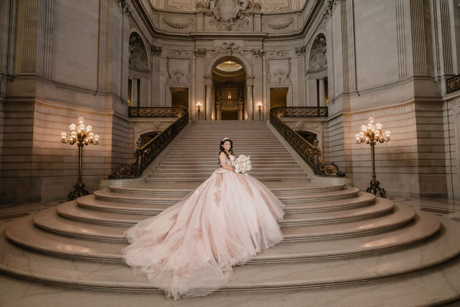 Dramatic quinceanera portrait featuring a pink ballgown on grand marble staircase with elegant lighting.