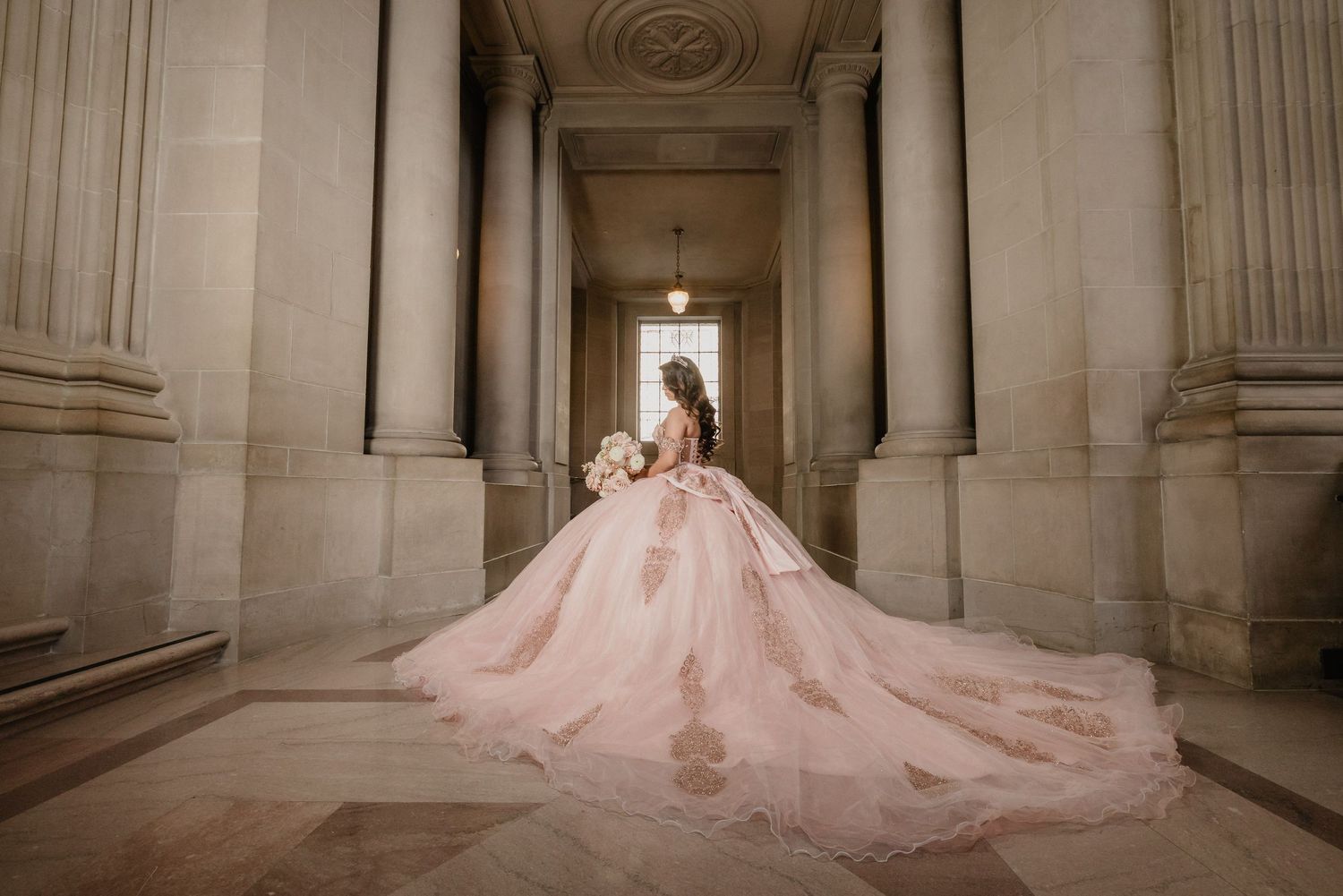 Dramatic silhouette of bride in pink gown with cathedral train between classical columns.