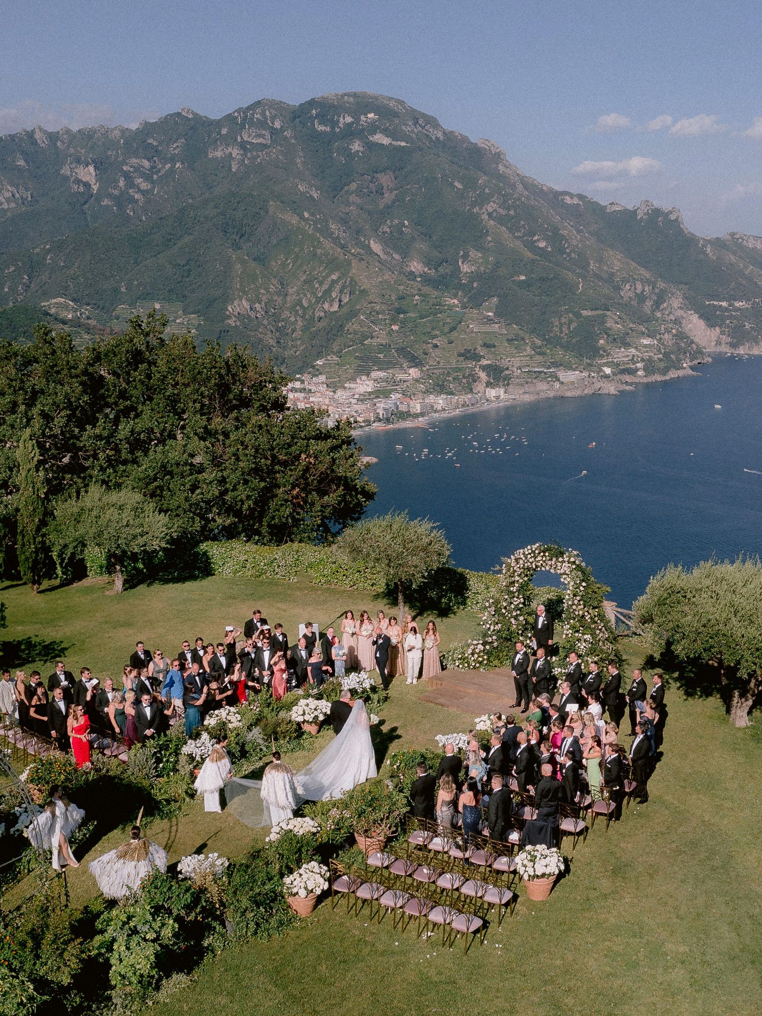 Outdoor wedding ceremony at Villa Gimbrone overlooking the Amalfi Coast with guests gathered on a hilltop lawn by the Mediterranean Sea.