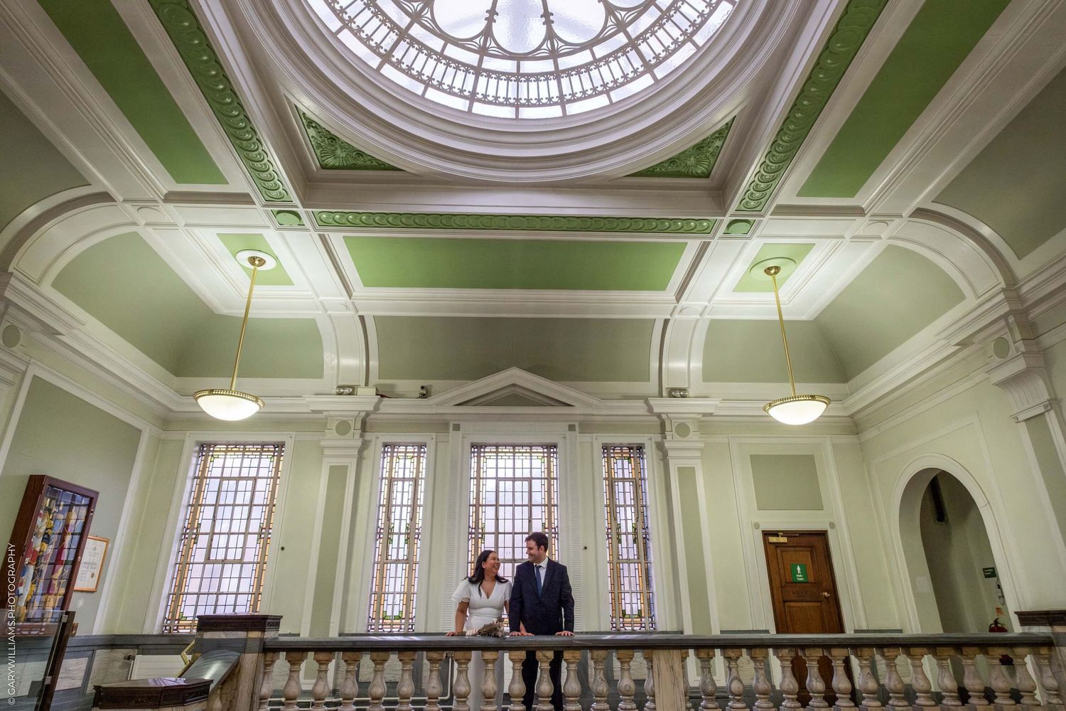 Architectural interior of a grand historic building with mint green walls and ornate dome ceiling with natural light.