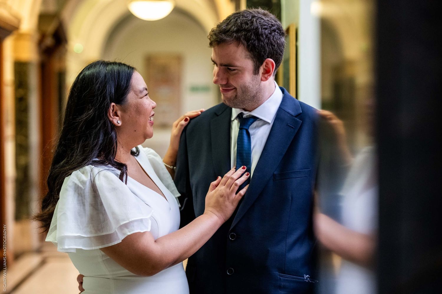 A happy couple laughs together in an elegant hallway with arched ceilings and warm lighting.