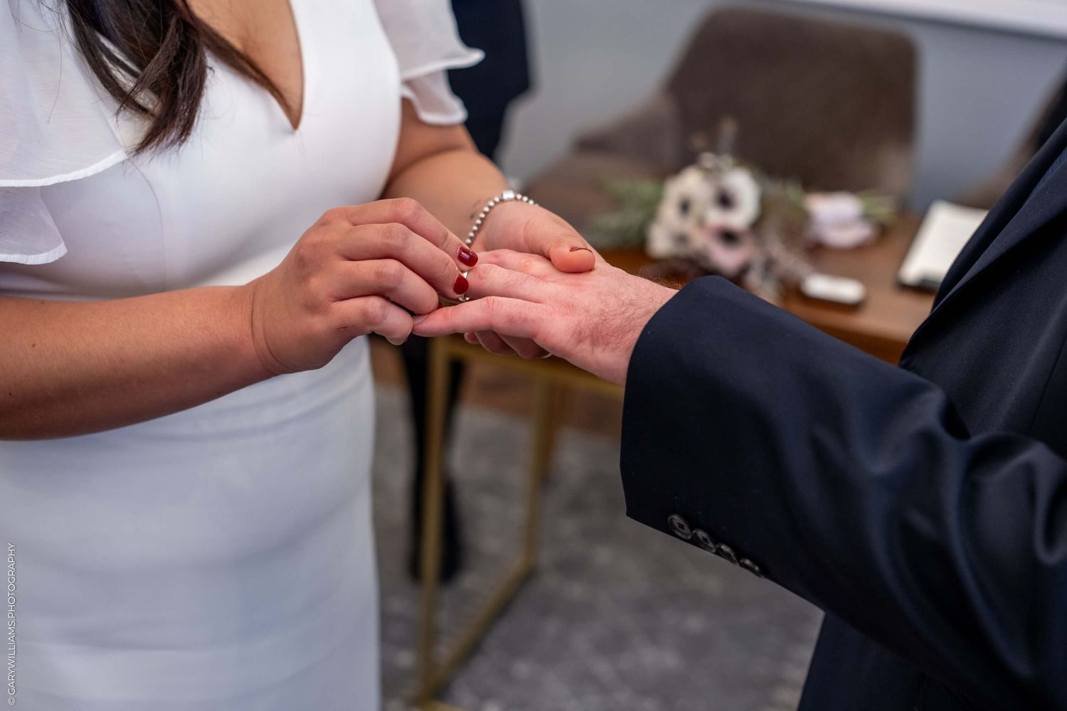 Close up view of hands during a wedding ring exchange ceremony against a blurred background.