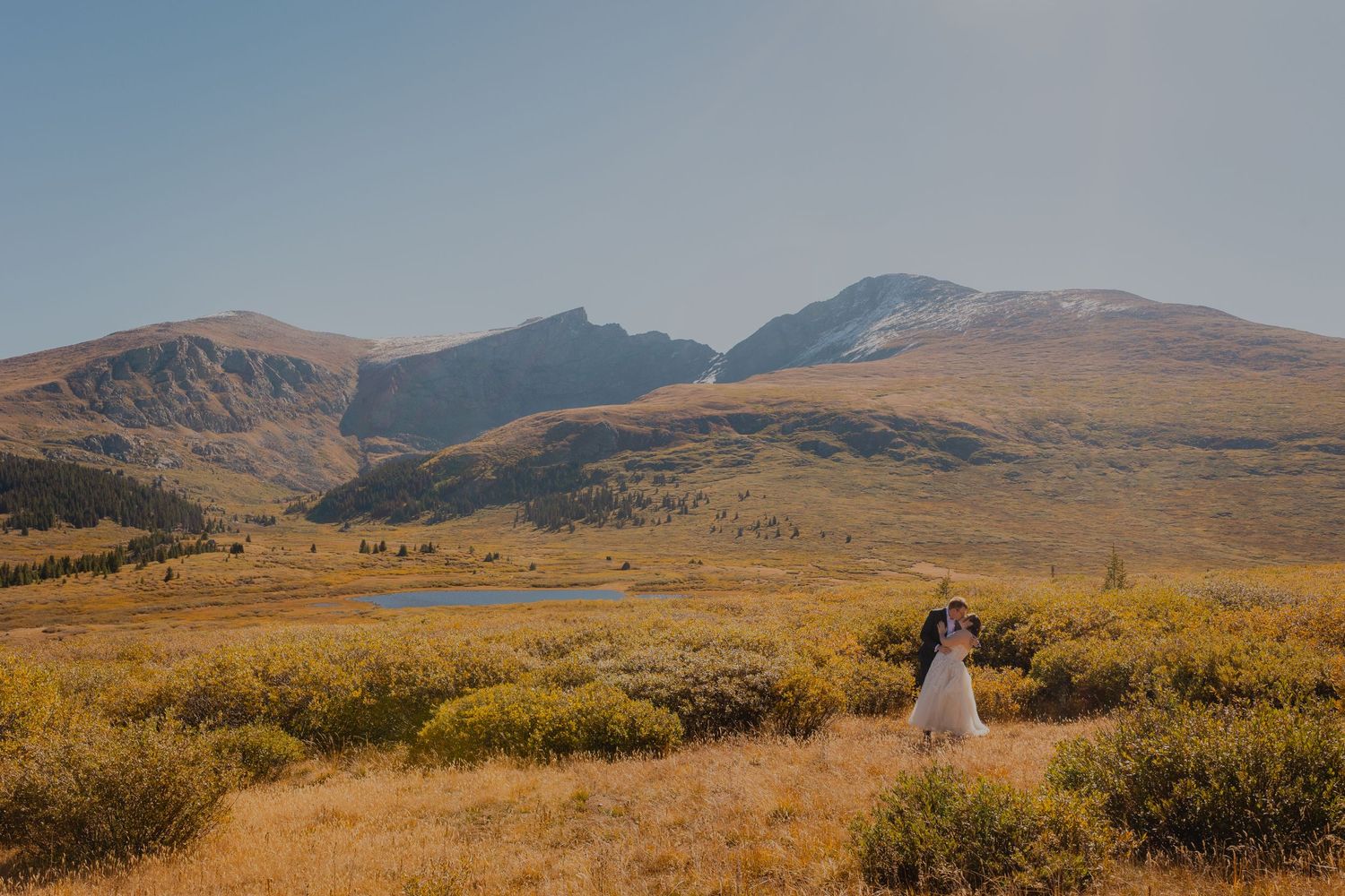 Scenic mountain landscape with couple walking down dirt path through golden autumn fields.