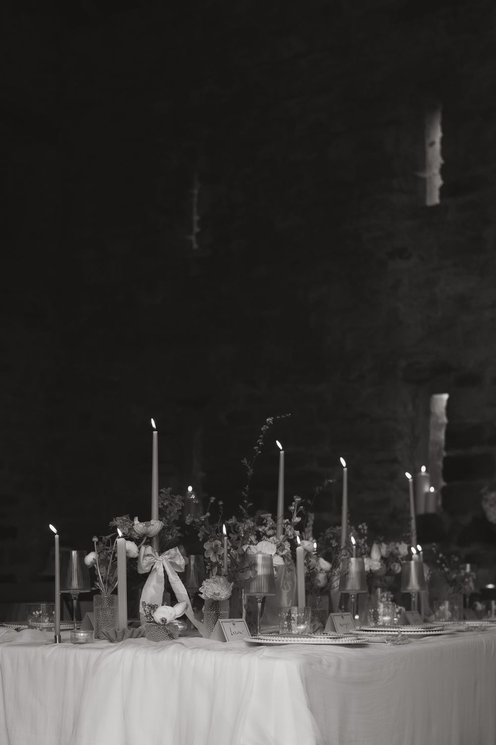 Elegant black and white party table setting with tall white candles and floral arrangements on white tablecloth.