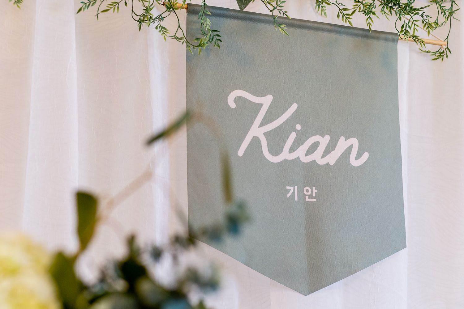A frosted glass sign displays 'Kian' in both English and Korean text, with delicate green foliage visible in the background.