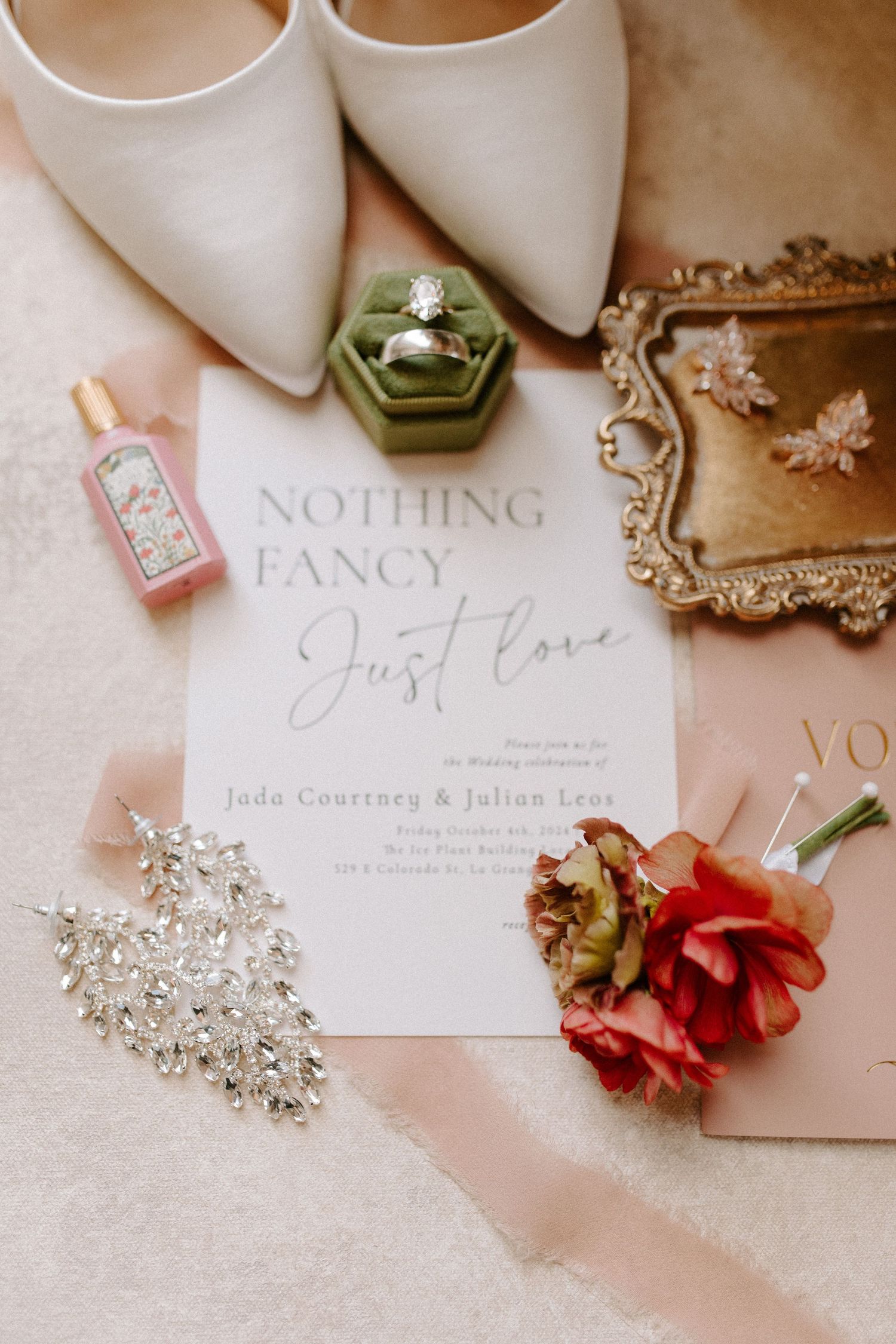 Wedding details flat lay with white shoes, invitation, rings in green box, and pink florals.