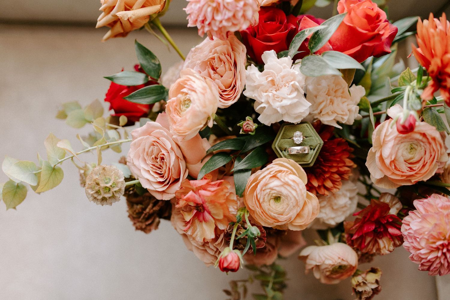 Wedding floral arrangement featuring peach roses and red blooms with green accents.